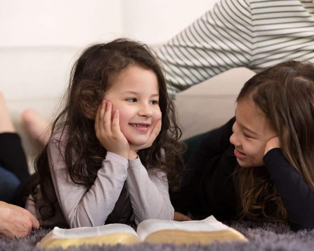 Image of two young children and parents sprawled on a rug, reading the Bible together.