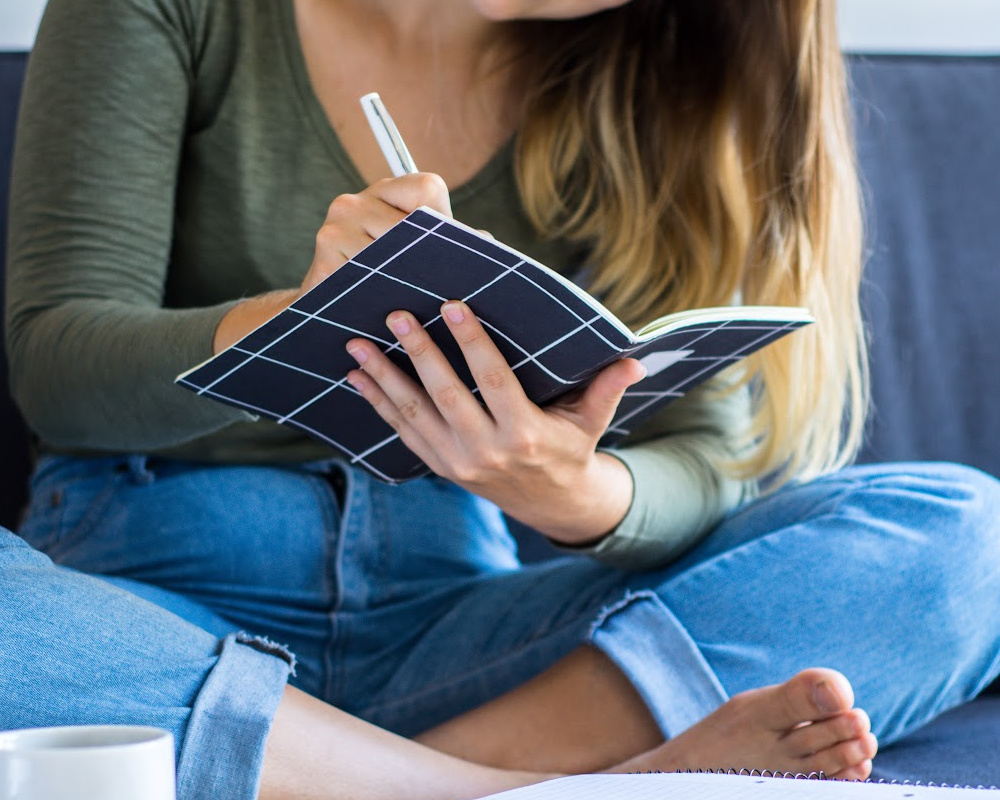 Woman writing in a journal and sitting on a couch.