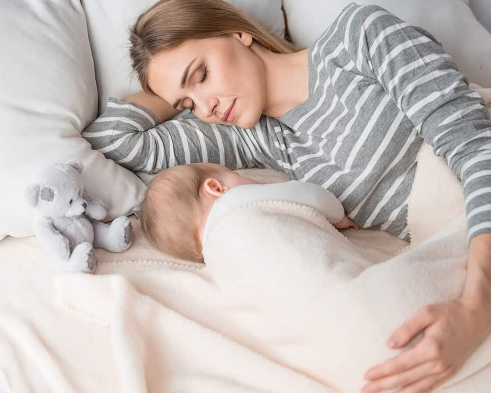 Image of mom and baby sleeping side by side in a bed; concept of sleep deprivation with several children at home.