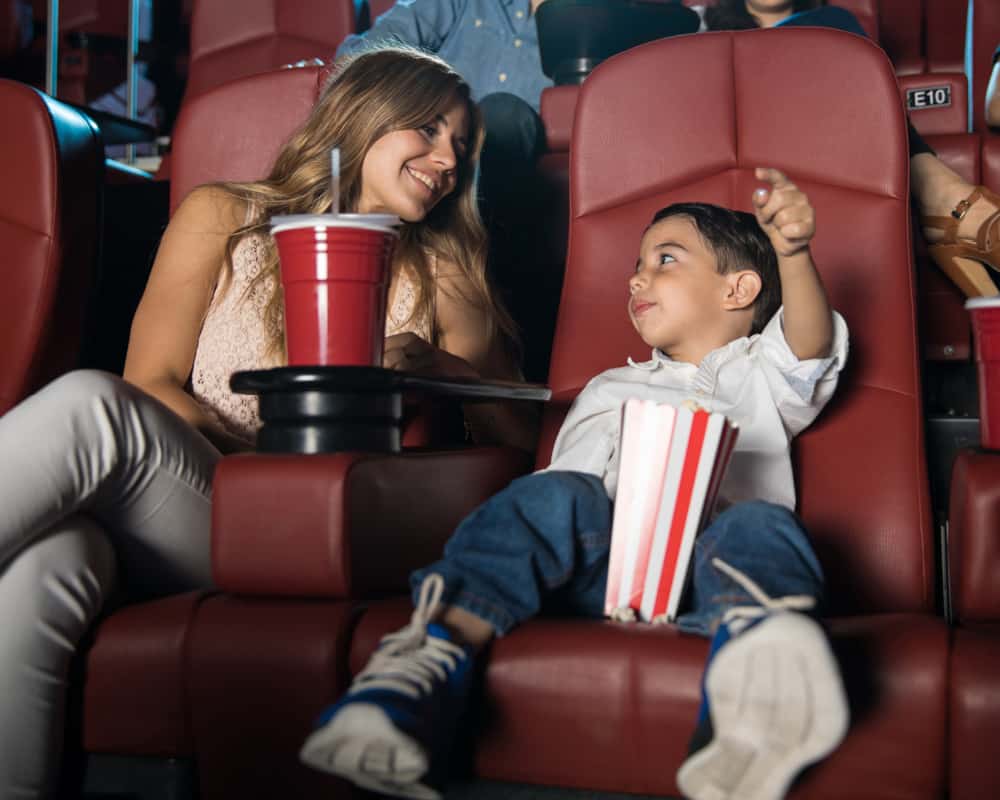 Image of a young mom and her preschool-aged son sitting in a movie theater, talking. Concept of taking kids in public.