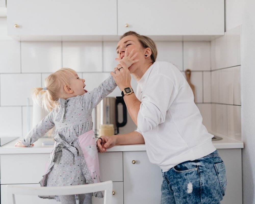 Mom in kitchen with toddler daughter, playing a silly game together.