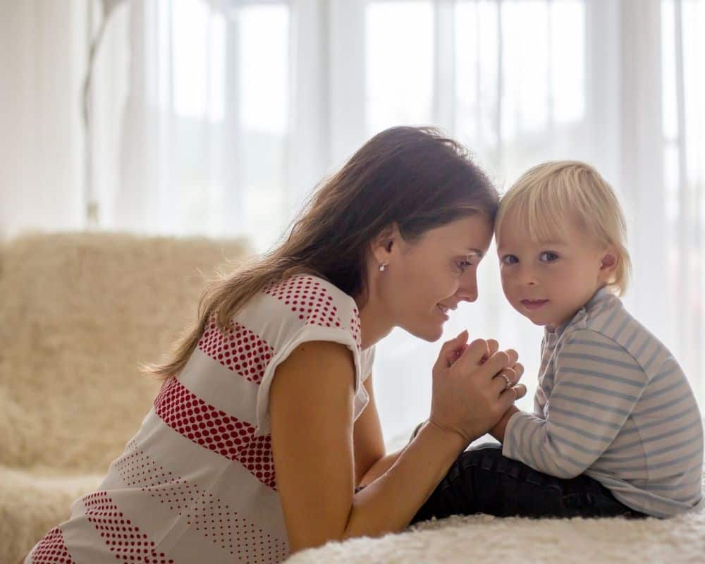 Image of mom kneeling and prayer with hands clasped around her toddler son's hands.