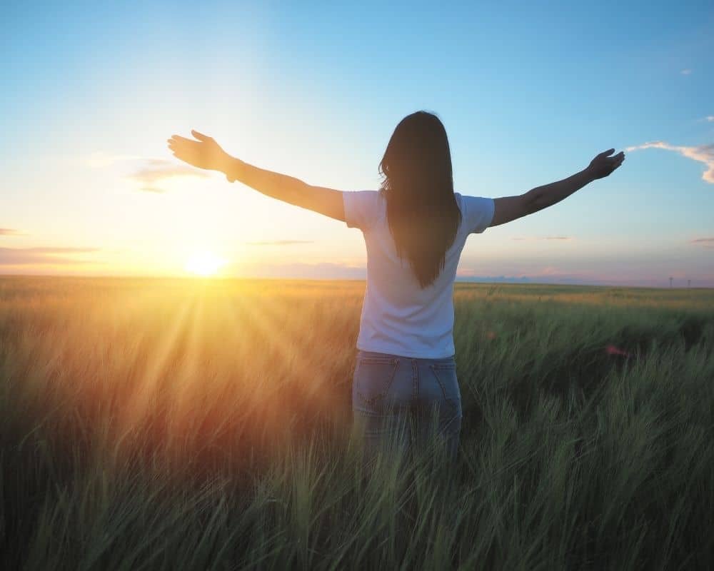 Woman standing in a field with her hands up to the sky, praising God.