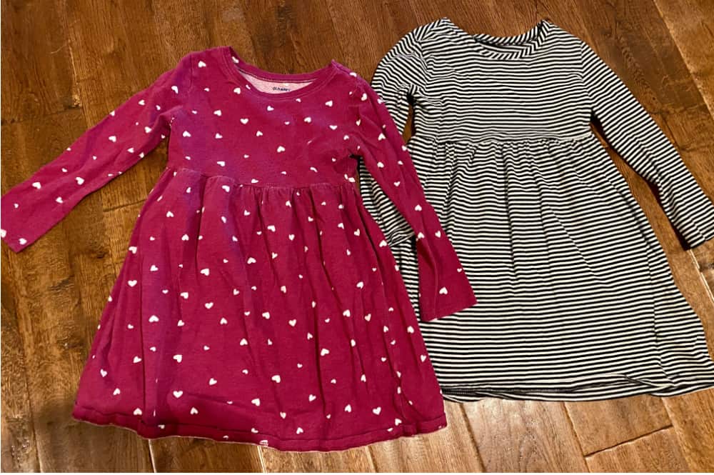 Image of a pink toddler dress with hearts and a black-and-white striped toddler dress side by side on a wooden floor. Concept of selling clothing lots versus single items on Marketplace.
