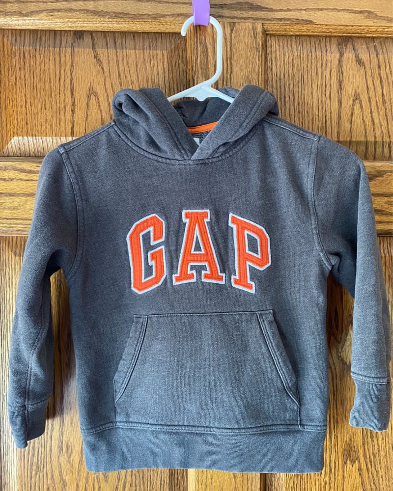 Image of boy's GAP hoodie hanging against a wooden door, depicting an example of natural lighting and bright photos as important to consider for listing items to sell online.