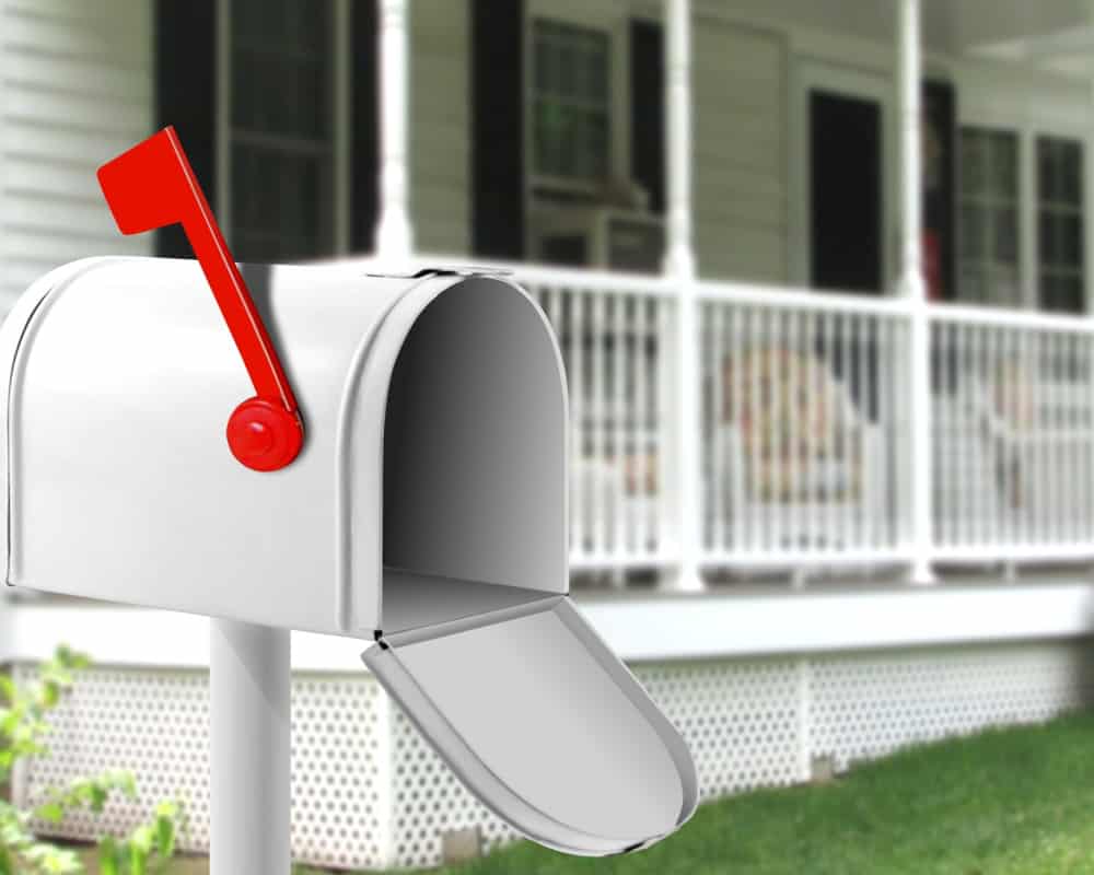 Image of open mailbox with white house with wraparound porch in the background. Concept of shipping items and making money from Facebook marketplace without leaving home.