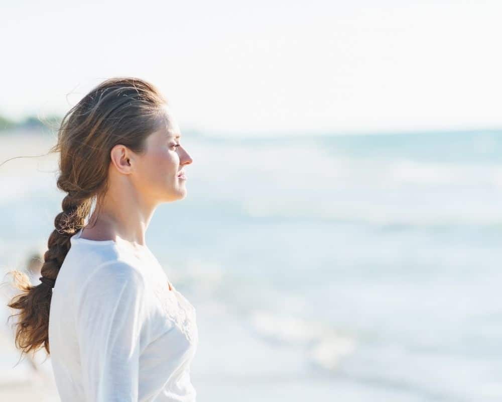 Woman calmly looking out over the ocean, standing on a beach. Concept of using Bible verses about worry for strength.