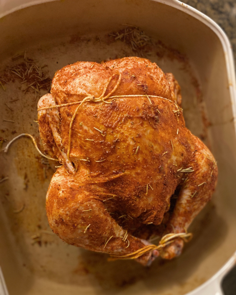 Whole free range chicken rubbed with spices and ready to roast, in a white pampered chef stoneware baking dish. 