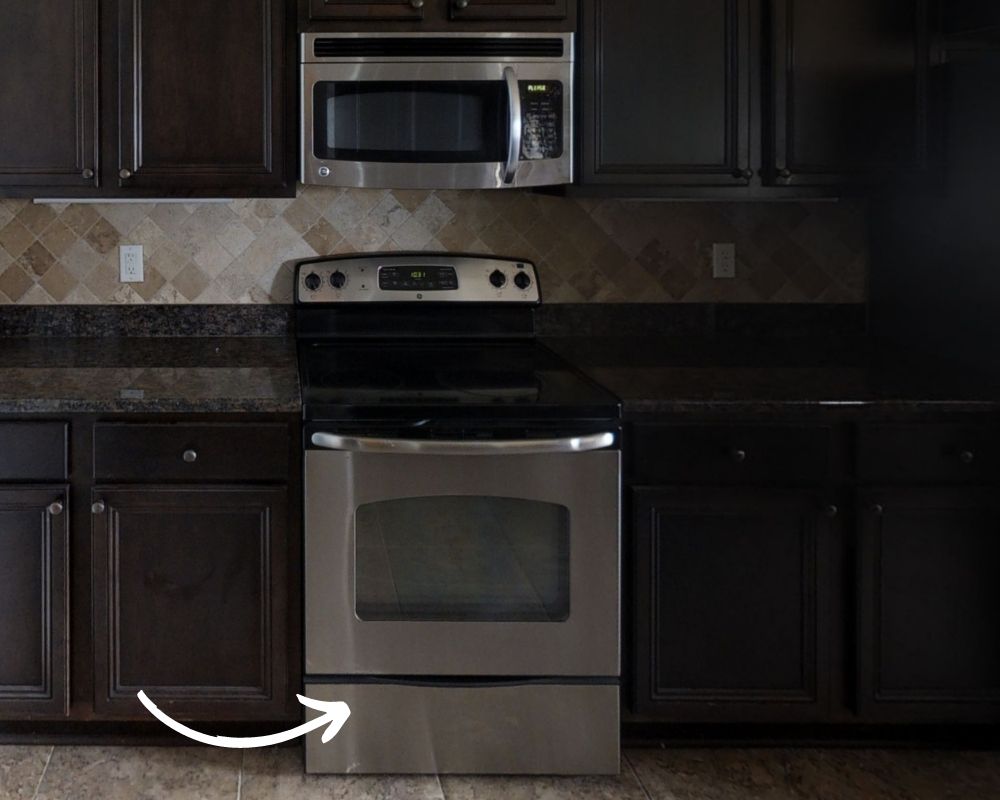 Stainless steel stove in a modern kitchen with an arrow pointing to the bottom warming drawer.