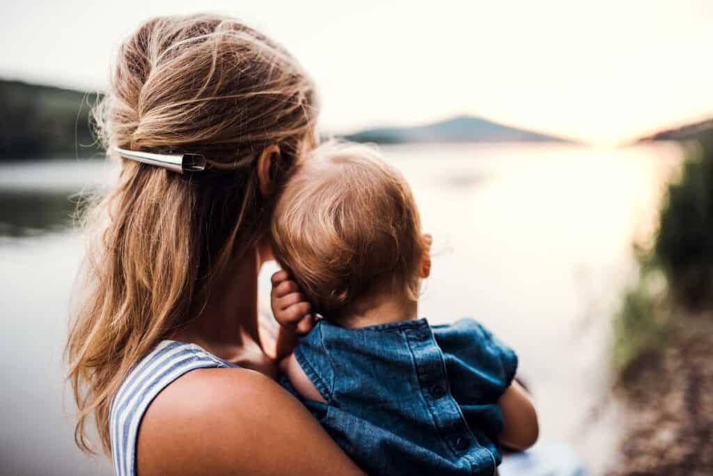Young mom holding baby boy outside overlooking a lake.