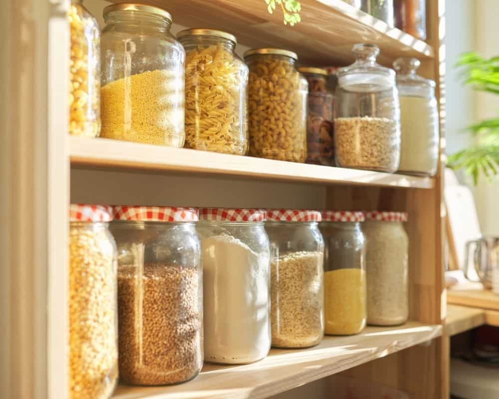 Glass food jars on a pantry shelf with bulk food items stored inside.