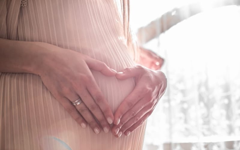 An expectant mother holding her hands over her stomach in the shape of a heart.