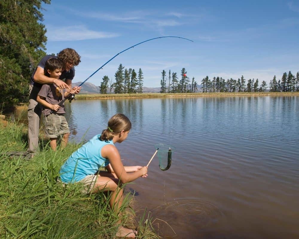 Dad and two kids fishing at a lake together.