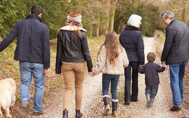 Three generations walking through a wooded path together in the fall.