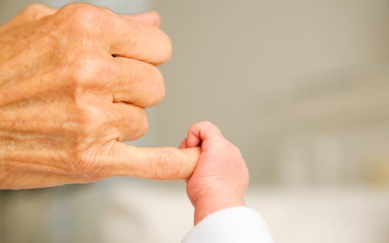 Grandmother's hand holding onto a baby's hand- concept of a grandmother's love for her grandchild.