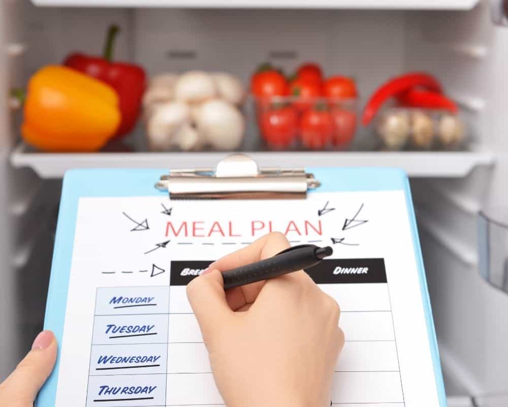 A woman writing a meal plan while looking through her refrigerator for inspiration.