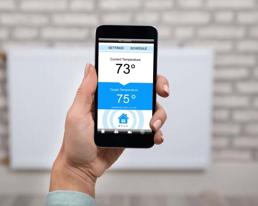 Woman holding a smartphone with a thermostat app.