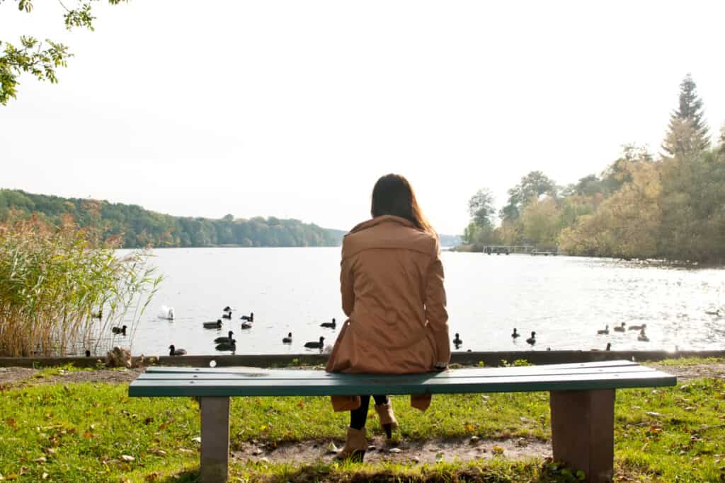 Woman sitting on a bench overlooking a pond, thinking.