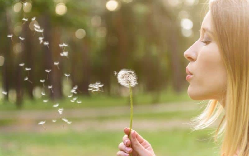 Woman blowing dandelion in the wind outside; concept of hope in struggle.