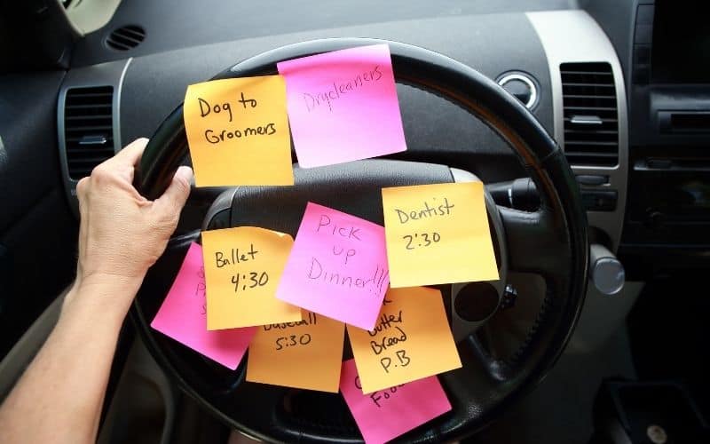 Steering wheel of car with sticky notes all over it with reminders of all the activities mom has to keep up with.