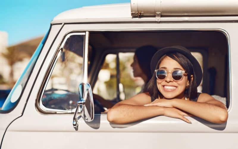 Teen girl smiling with her head propped on the window ledge of a car driving down the highway.