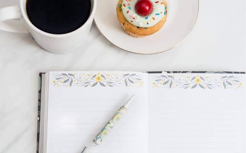 coffee cup, cupcake, an open notebook and pen set on a marble backdrop. Concept of making plans.