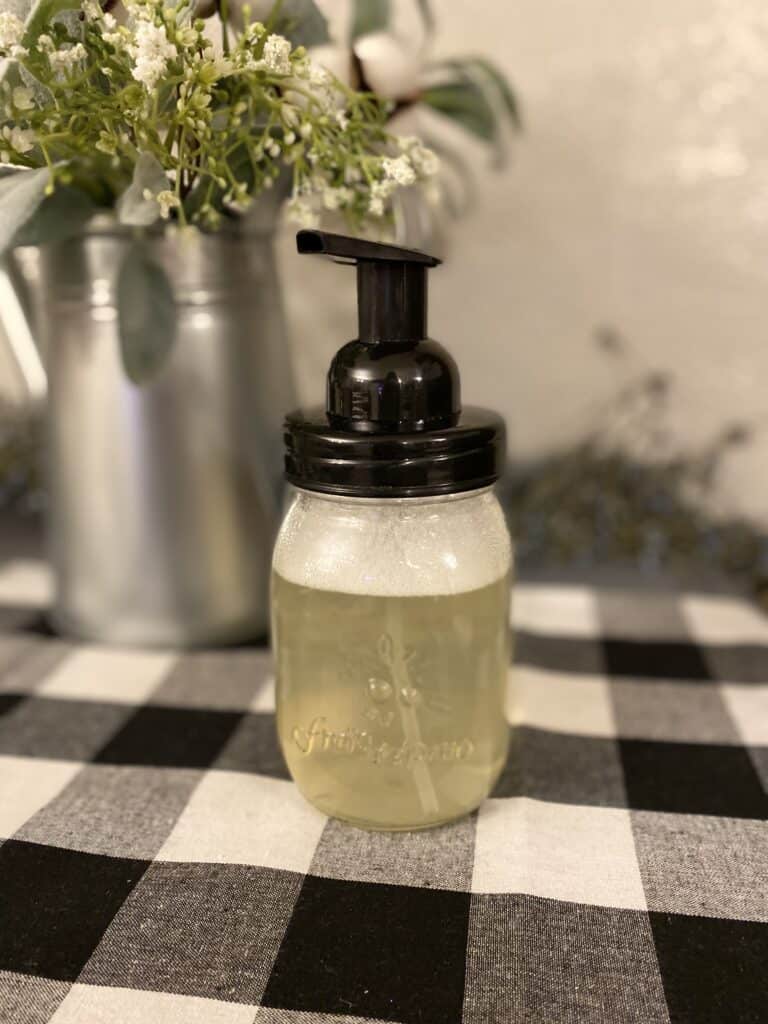 Image of glass foaming hand soap container on a buffalo plaid table runner.