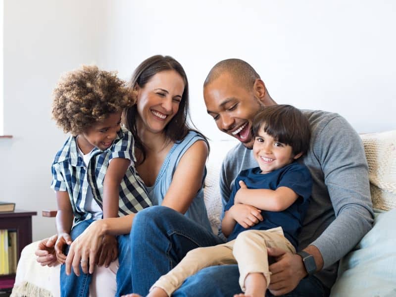 Mom, dad and two boys in living room, laughing. Concept of setting for Christian questions to ask kids.