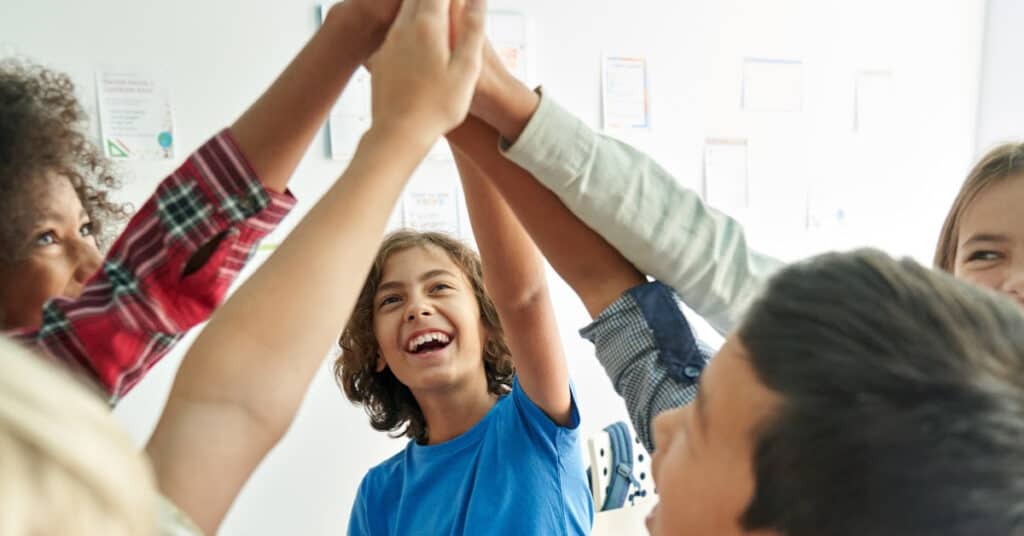 A group of kids smiling and high-fiving in a circle.