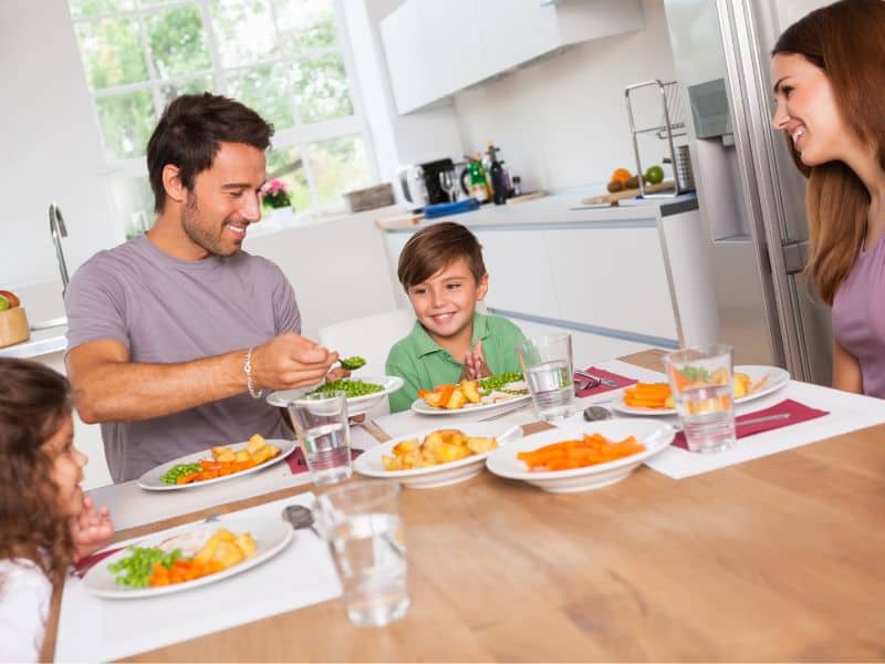 Family meal time with mom, dad and two kids. Concept of questions to ask kids about God around the dinner table.