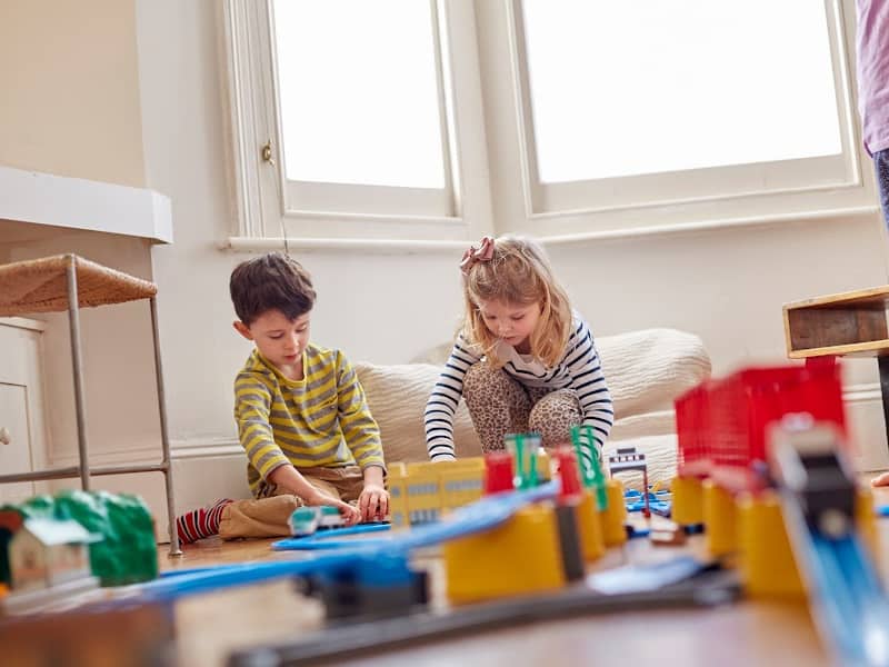Two siblings working together to build an elaborate train track in a playroom at home.