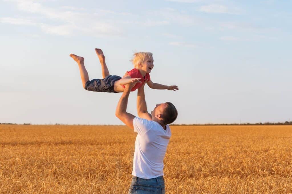 Young dad swinging little blonde boy through the air in a wheat field.