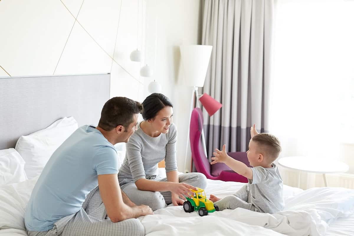 Mom and dad sitting in bed in toddler son's room, playing trucks with him before bedtime.