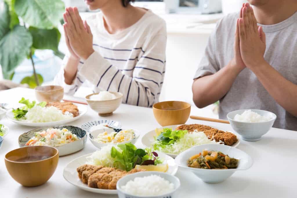 A husband and wife praying over a meal spread across a dinner table at home.