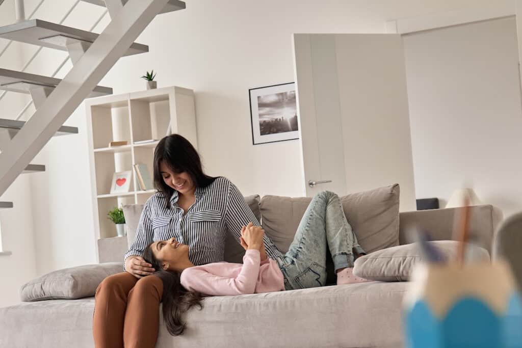 mom and teen daughter spending time together on the couch, with daughter's head in her lap, both smiling.