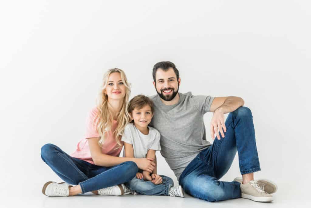 Mom, dad and young son sitting on the floor together, smiling.