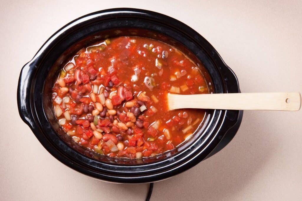 three bean chili in an open crockpot with a wooden spoon.