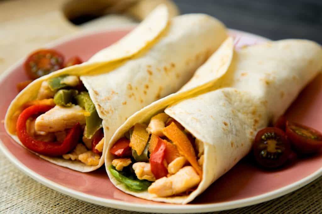 Two chicken fajitas on a pink plate.