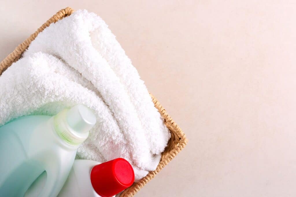 Basket with clean white towels, laundry soap and fabric softener.