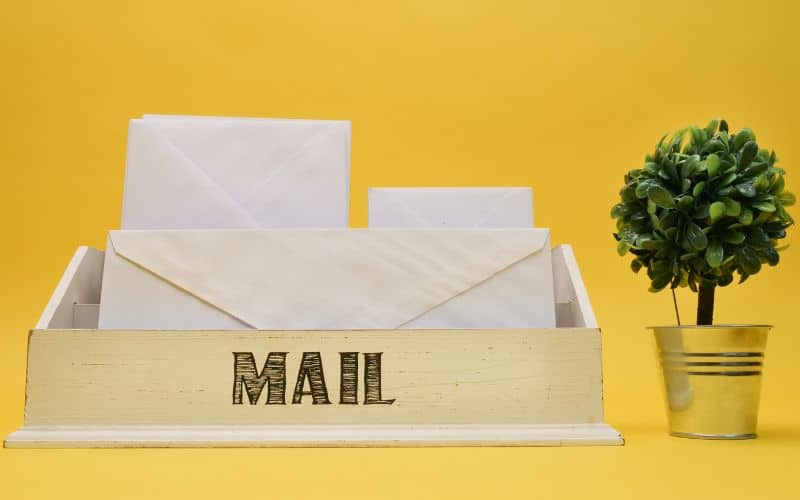 Wooden mail organizer box labeled "Mail" with a faux topiary plant sitting on a desk with a yellow background.
