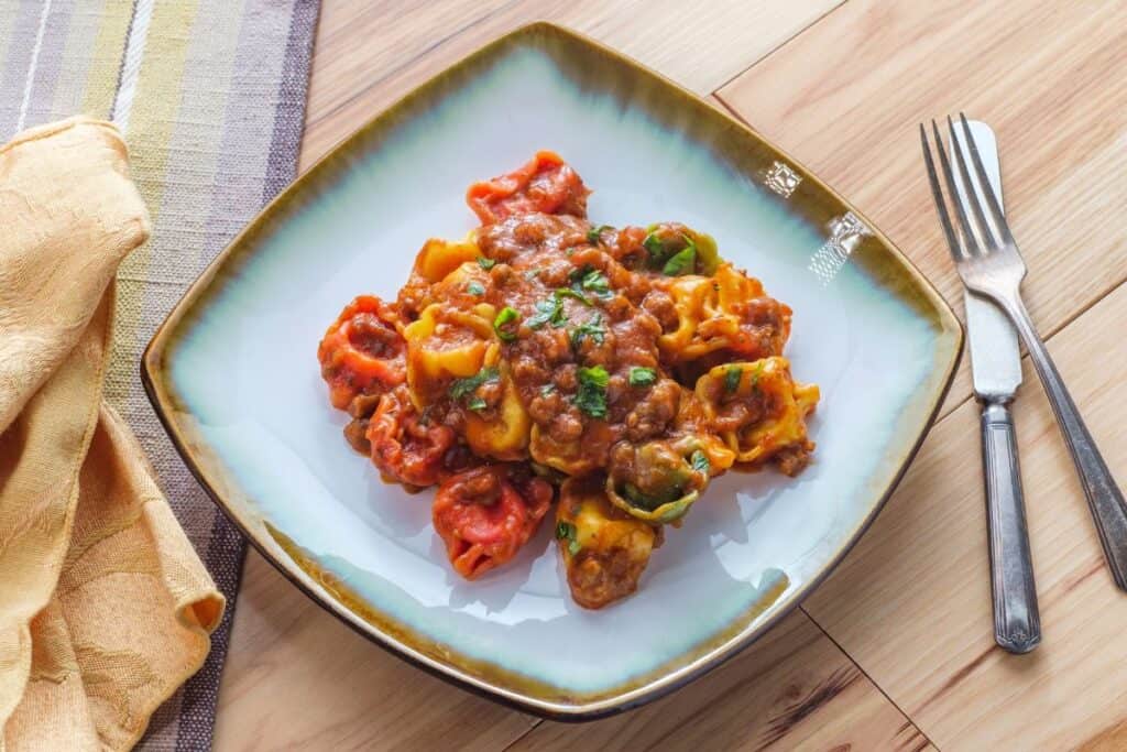 A plate of tortellini with red sauce on a square plate sitting on a wooden table.