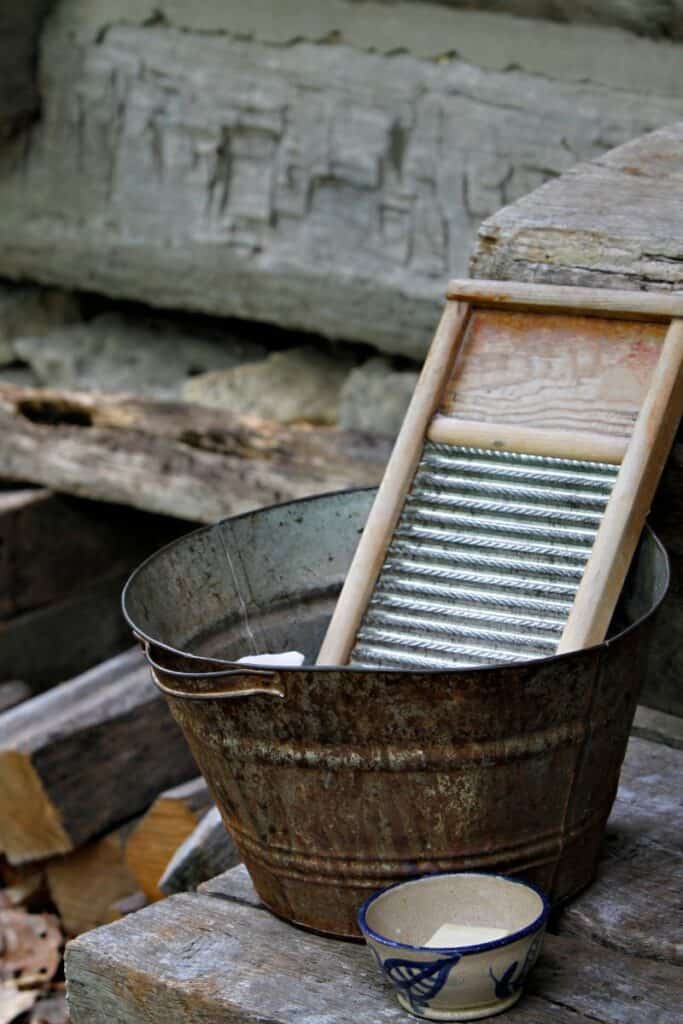 Old fashioned washboard in a metal washing bucket on a weathered wooden table outside.