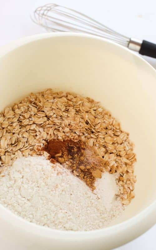 Dry ingredients for oatmeal gingerbread cookies in a white bowl, ready to whisk.
