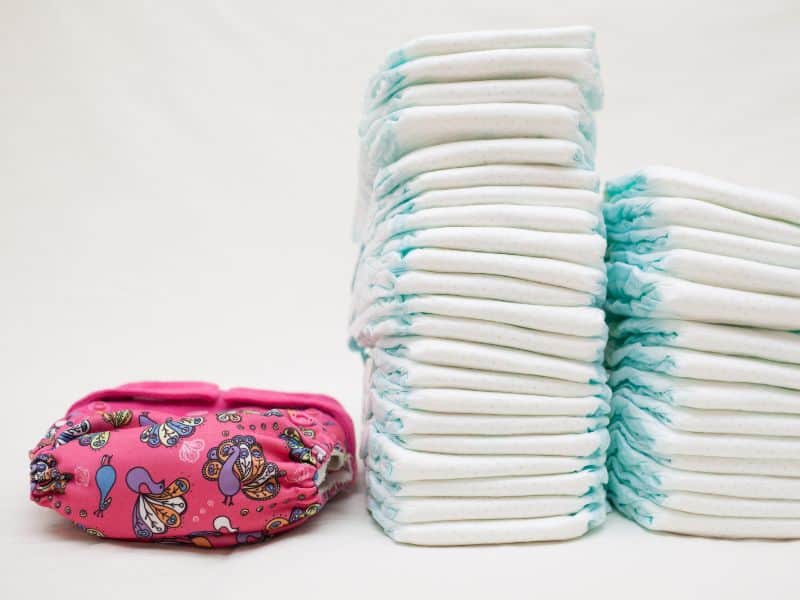 One pink cloth diaper on a white background, with two stacks of disposable diapers beside it.