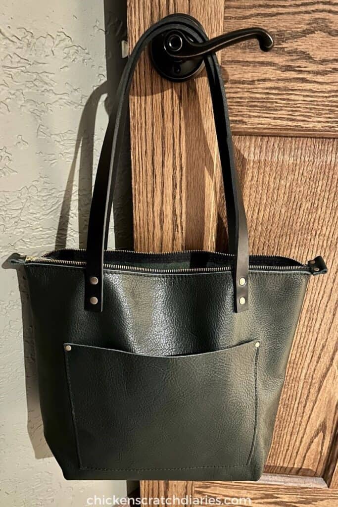 Forest green Portland Leather goods tote bag hanging on a door handle of a wooden door. Great gift idea for practical women.