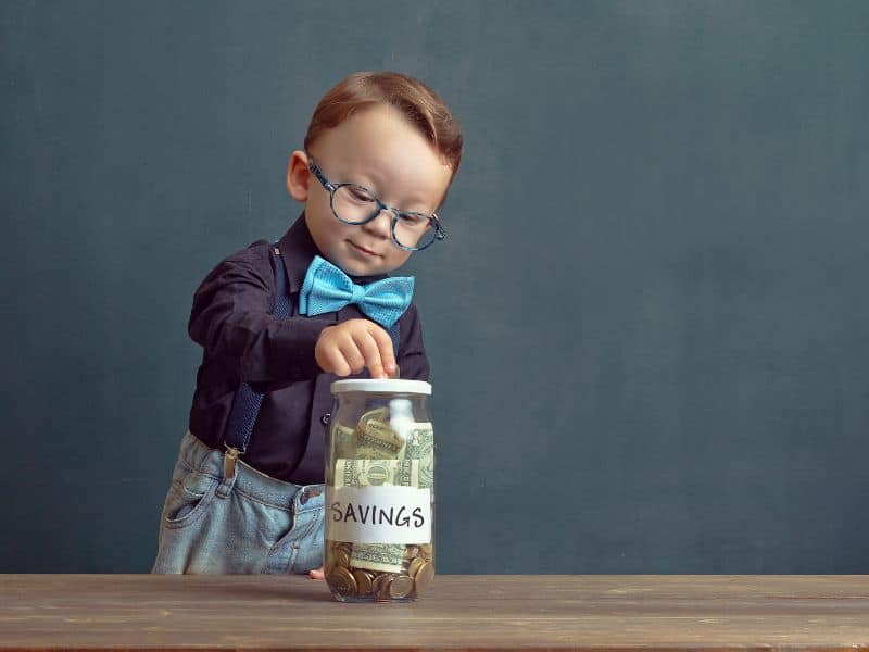 preschool child wearing glasses and adding money to a large glass jar labeled savings