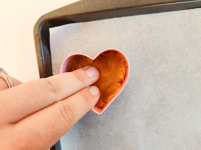 Pressing the peanut butter cookie dough into the mini heart shaped mold on a parchment-lined cookie sheet.