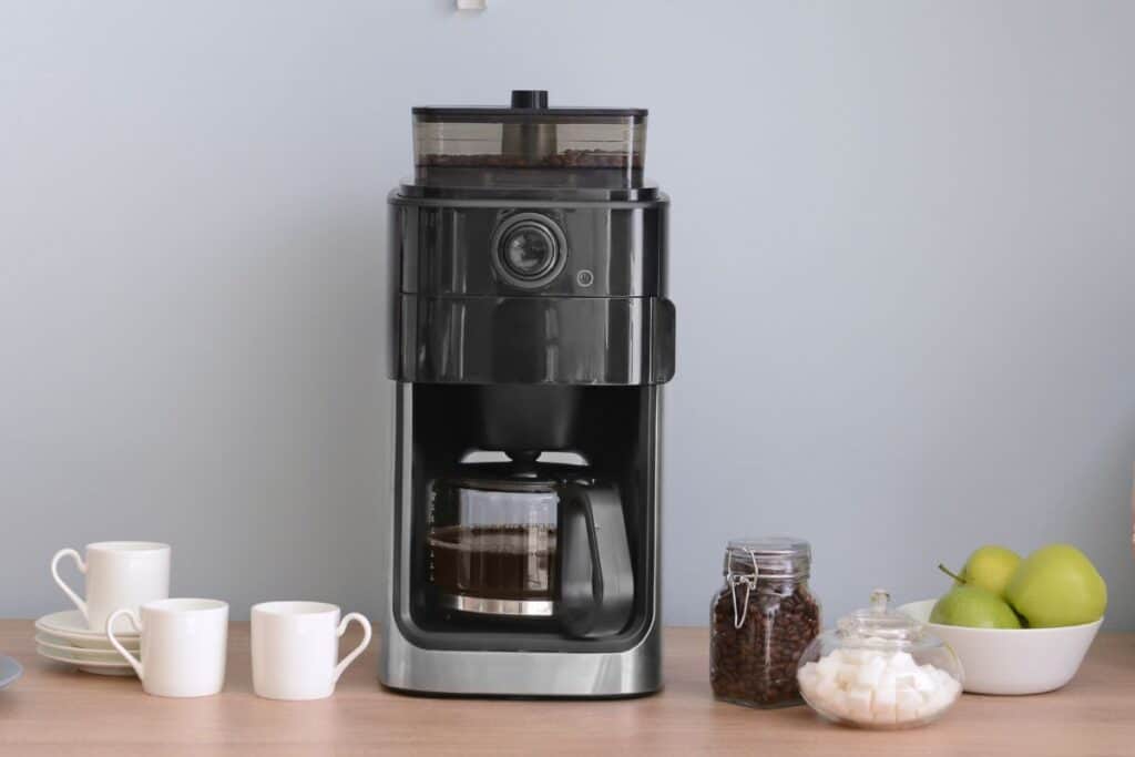 Brewed pot of coffee on a wooden countertop with coffee accessories, cups and sugar cubes nearby.