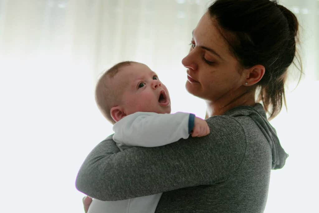 exhausted new mom walking the floor with newborn baby boy in a dimly lit room.