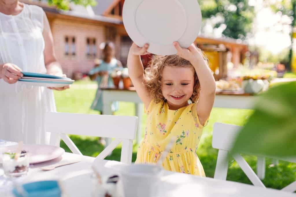 Little girl in a yellow dress setting a plate on an outdoor table at a party.